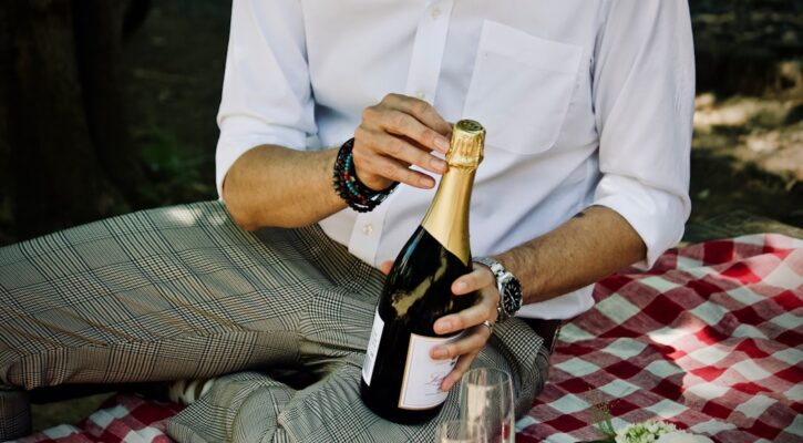 Person's hands hold two different wine bottles, one with a simple label and one with a luxury label, comparing them in a b...
