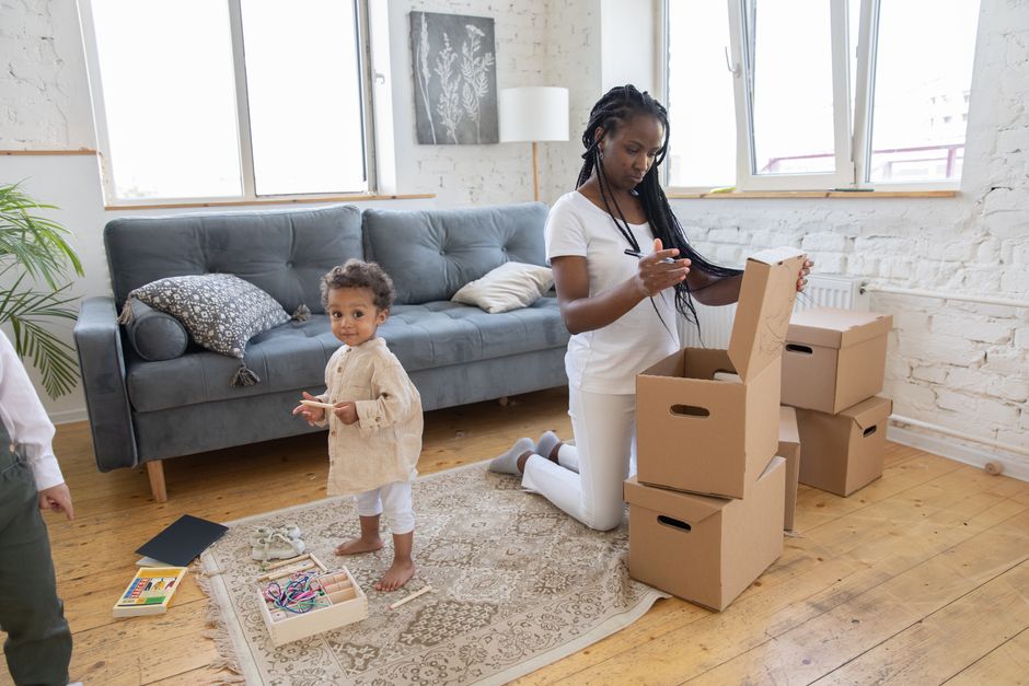 A woman smiling peacefully on a sofa in a bright, airy living room with a few neatly packed moving boxes, symbolizing a calm and organized home selling process.